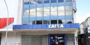 Fachada de agência da Caixa Econômica Federal com portas fechadas e cartazes vermelhos com a palavra greve colados na porta de vidro