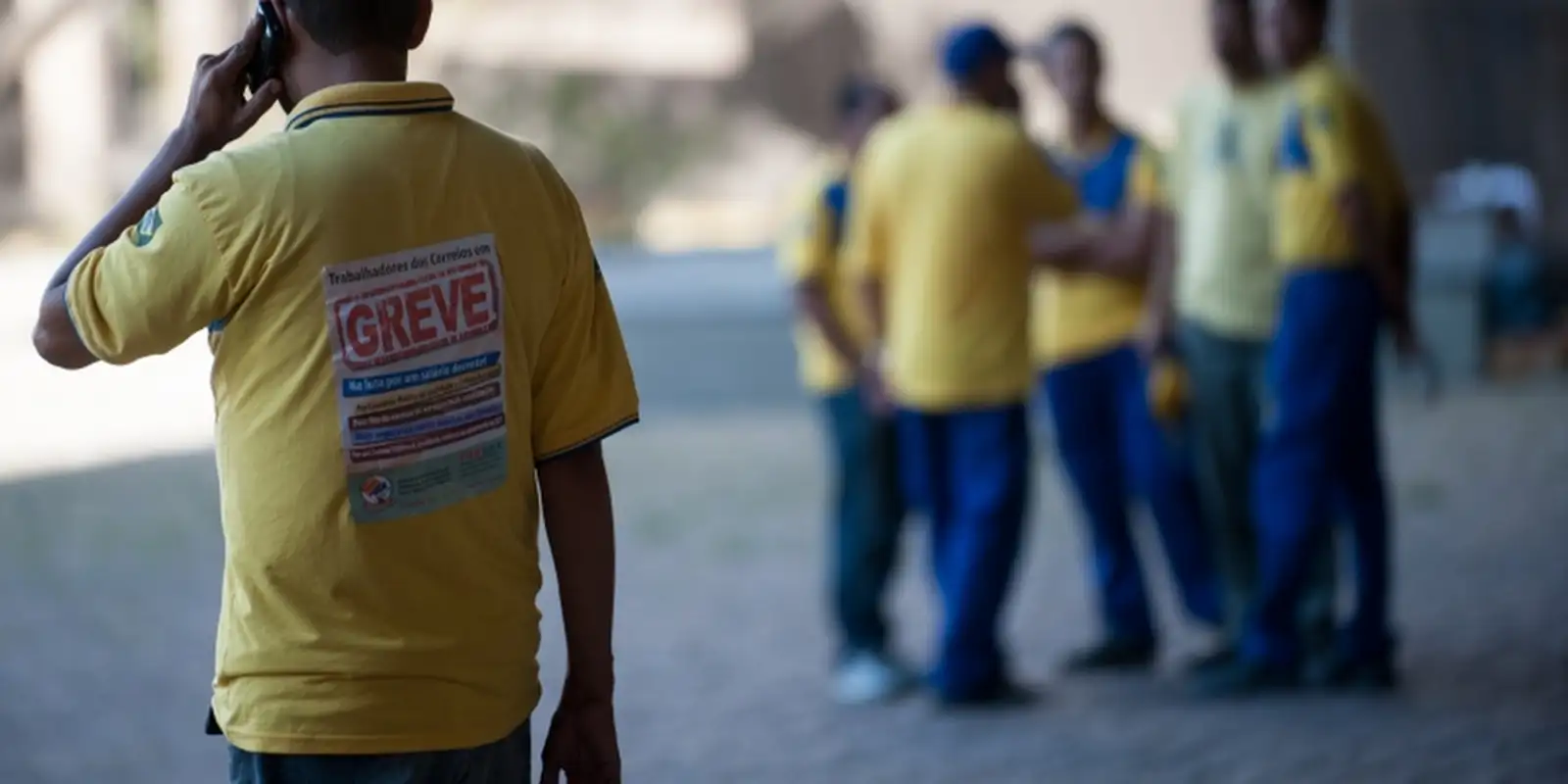 Trabalhador dos Correios de uniforme amarelo com cartaz de greve nas costas