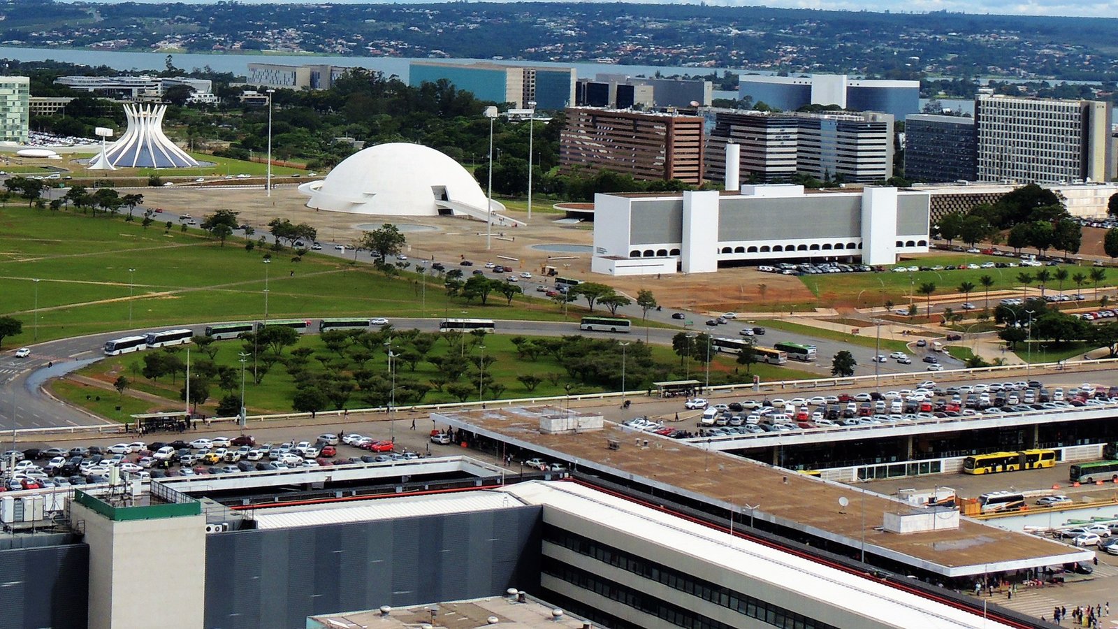 Vista aérea da Rodoviária do Plano Piloto, com ônibus na plataforma e no Eixo Monumental, e a Catedral de Brasília ao fundo
