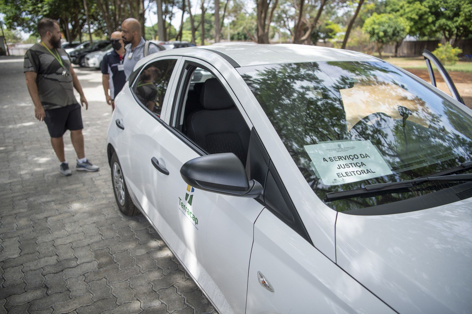Carro branco com cartaz no para-brisa escrito a serviço da Justiça Eleitoral