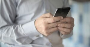 Pessoa de camisa social segura um smartphone com as duas mãos
