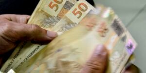 Mãos contando cédulas de cinquenta reais