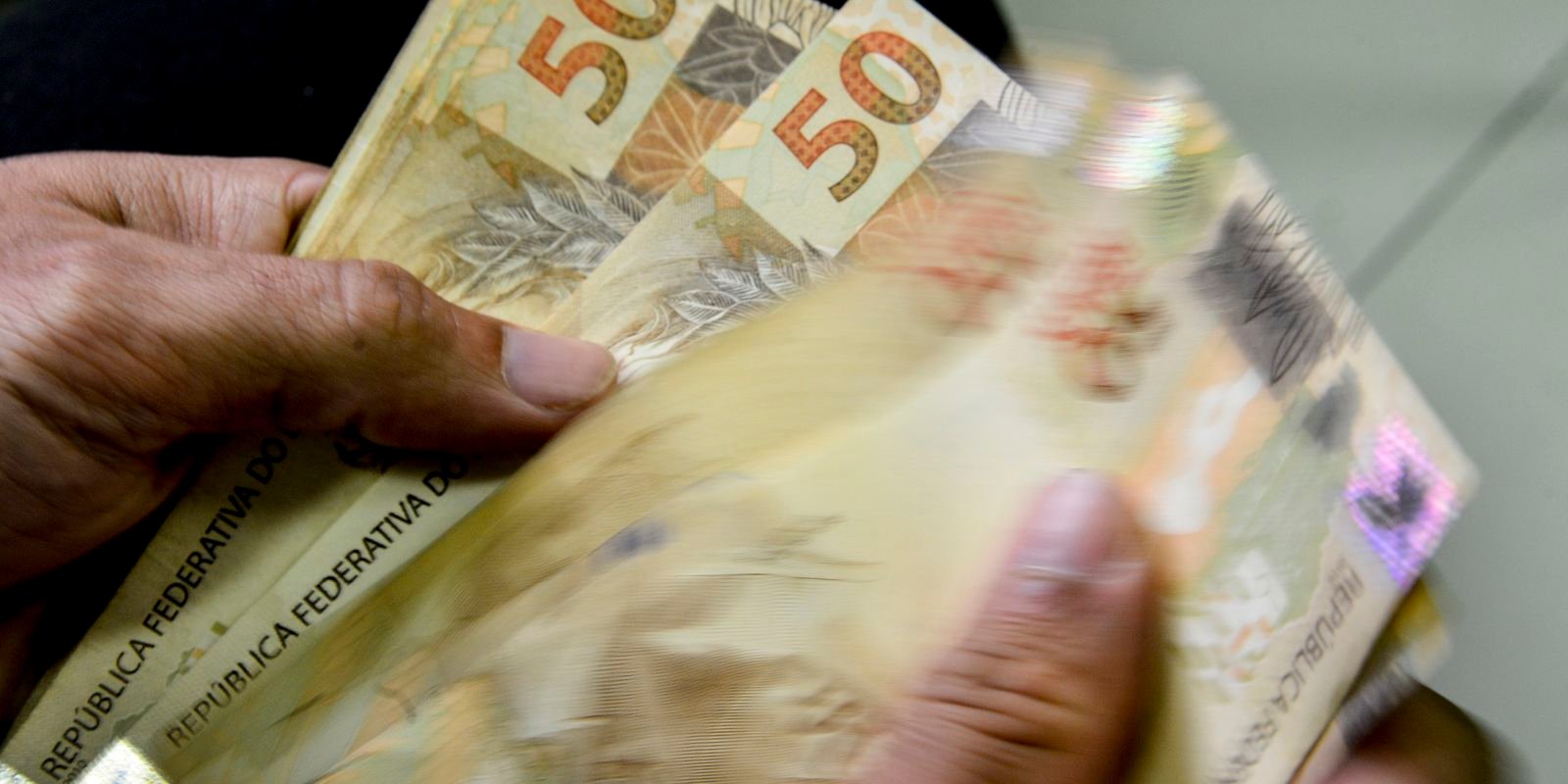 Mãos contando cédulas de cinquenta reais