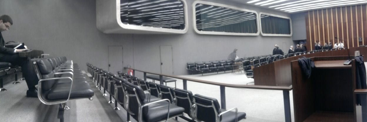 Plenário de julgamento do TJDFT com fileiras de cadeiras vazias e pessoas de toga ao fundo