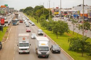 Avenida movimentada em Taguatinga, no Distrito Federal, com ônibus, caminhões e comércio nas laterais
