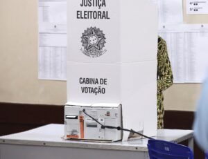 Cabina de votação da Justiça Eleitoral com urna eletrônica sobre a mesa em seção eleitoral