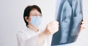 Médica de jaleco branco observa uma radiografia de tórax contra a luz em ambiente clínico