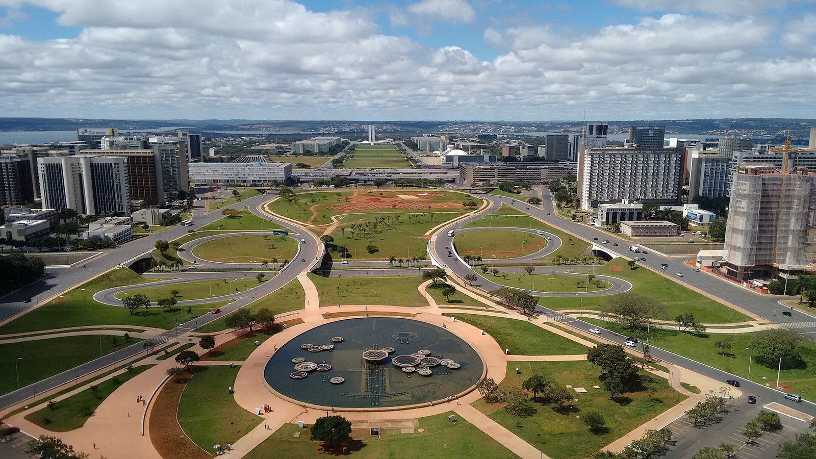 Vista aérea do Eixo Monumental de Brasília, com gramados, o espelho d'água da Torre de TV e o Lago Paranoá ao fundo