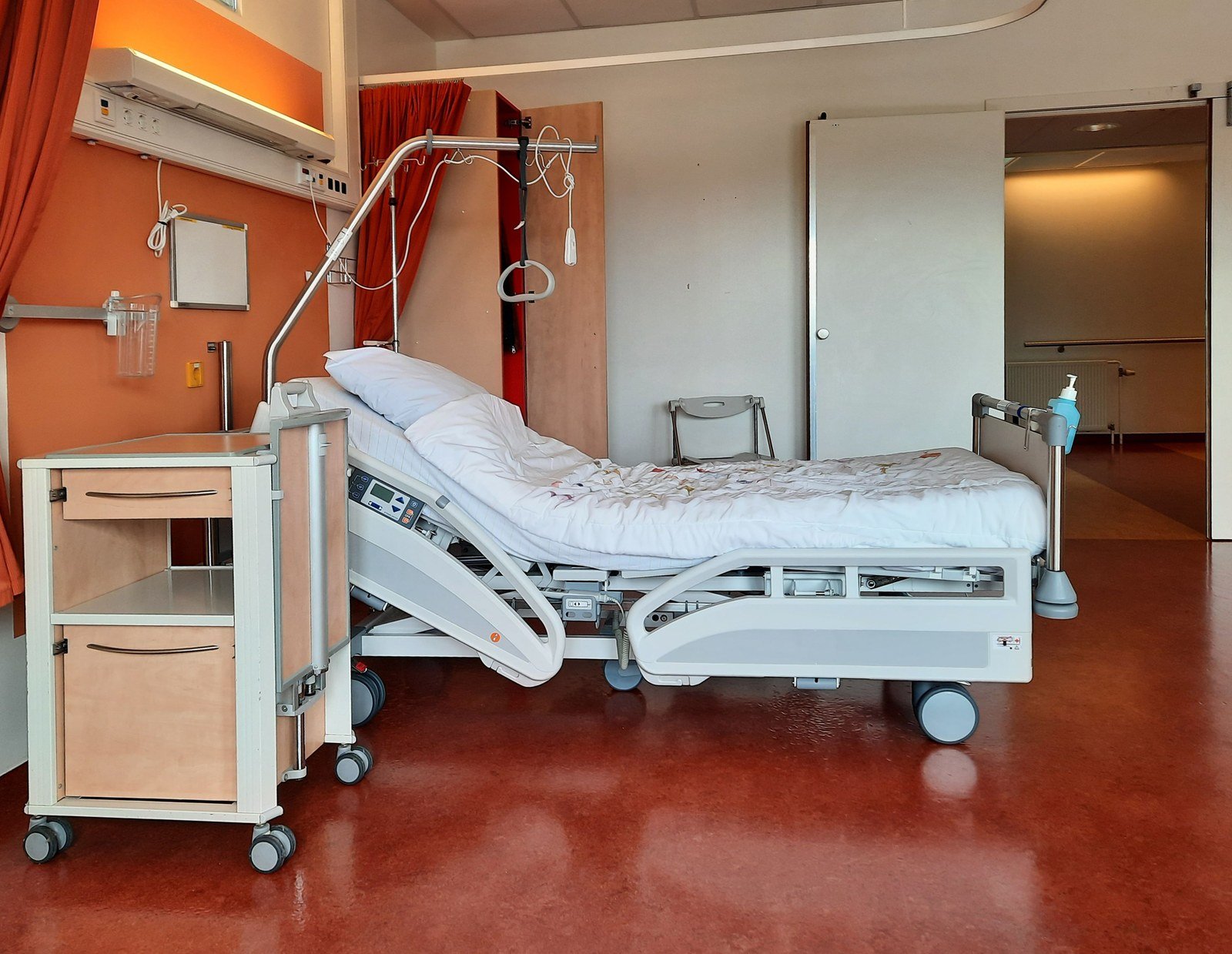 Quarto de hospital vazio, com leito articulado, criado-mudo e suporte de soro