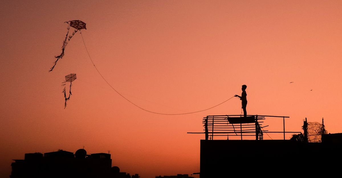 Silhueta de pessoa empinando pipa ao entardecer, com a linha esticada atravessando o céu