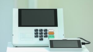 Urna eletrônica modelo UE2020 da Justiça Eleitoral, com teclado numérico e botões BRANCO, CORRIGE e CONFIRMA, ao lado do terminal do mesário