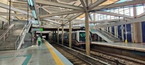 Trem do Metrô-DF parado na plataforma da estação Ceilândia Centro, com os trilhos em primeiro plano