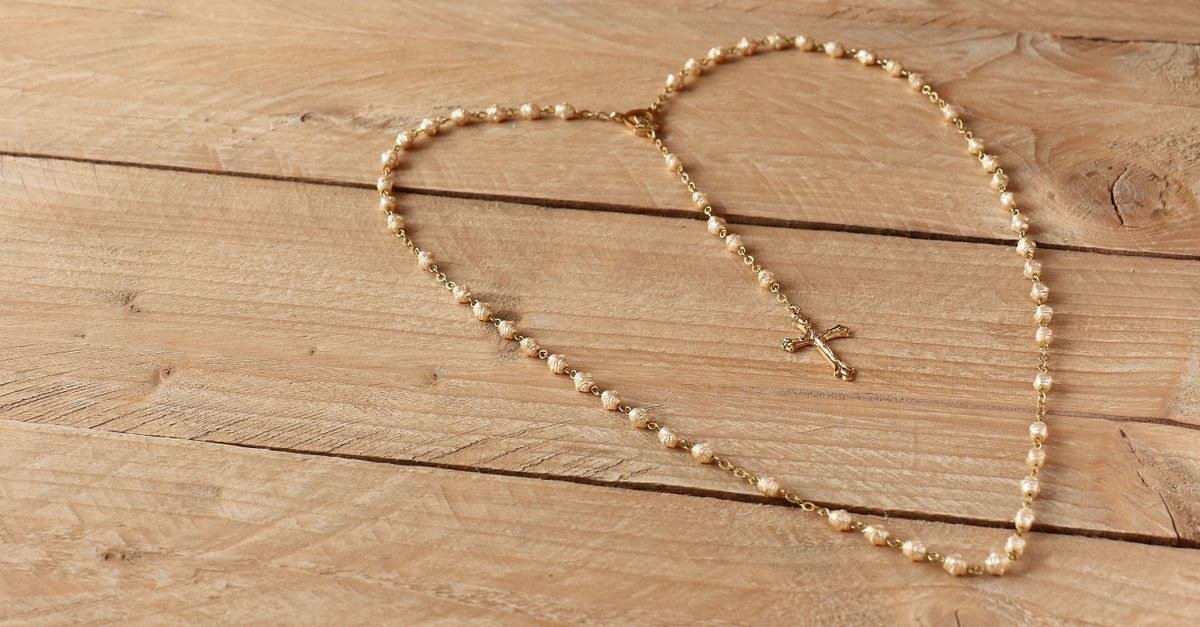 Terço dourado com crucifixo estendido sobre uma mesa de madeira clara