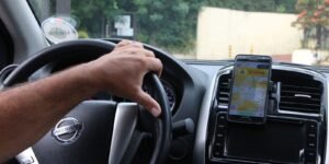 Motorista de aplicativo com a mao no volante e celular no painel exibindo o mapa da corrida