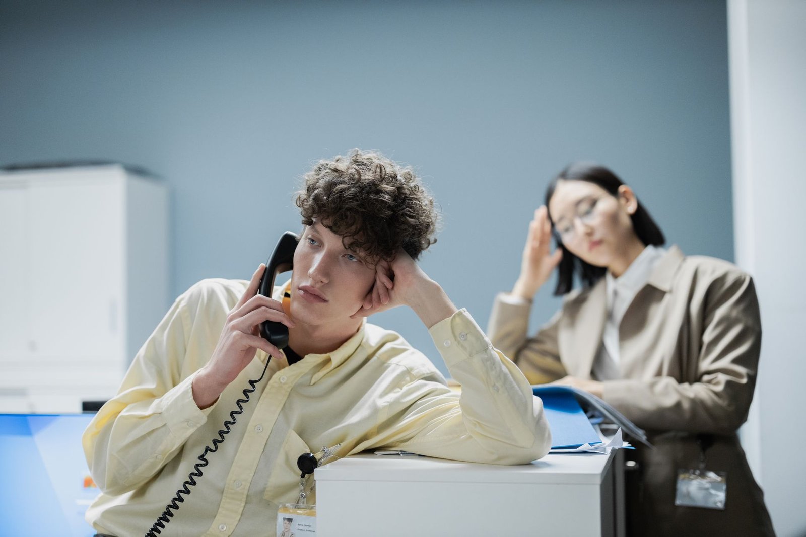 Dois trabalhadores de escritório com sinais de cansaço, um ao telefone e outro com a mão na cabeça