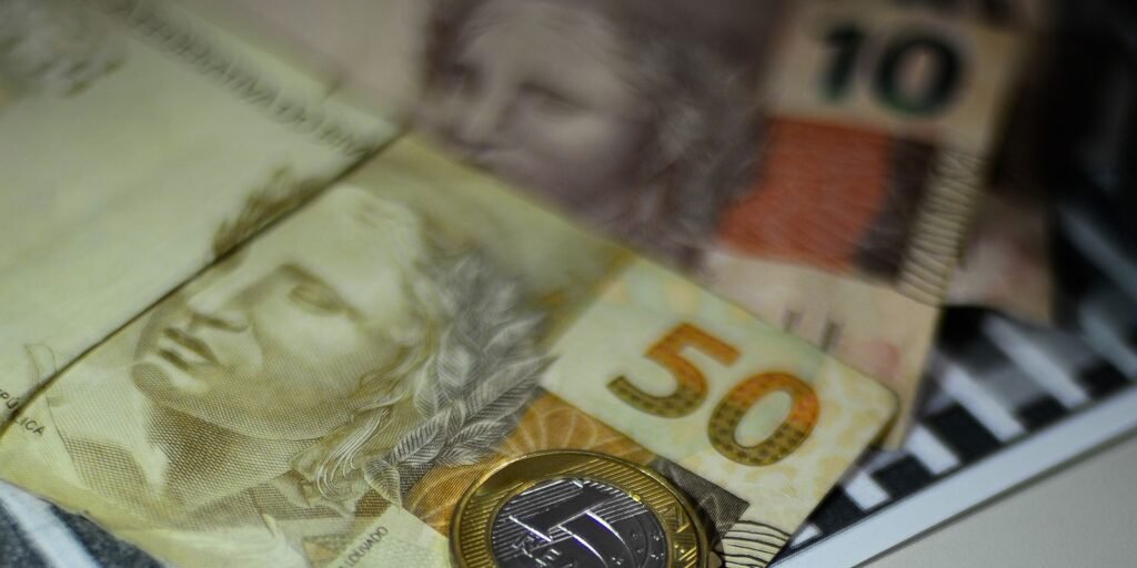 Cedulas de R$ 50 e R$ 10 e moeda de R$ 1 sobre mesa, em close