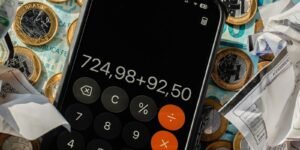 Celular com calculadora aberta sobre moedas de real, cédulas e notas fiscais amassadas