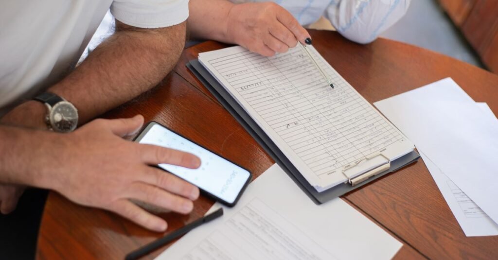 Duas pessoas conferem contas e documentos sobre a mesa com o auxílio da calculadora do celular