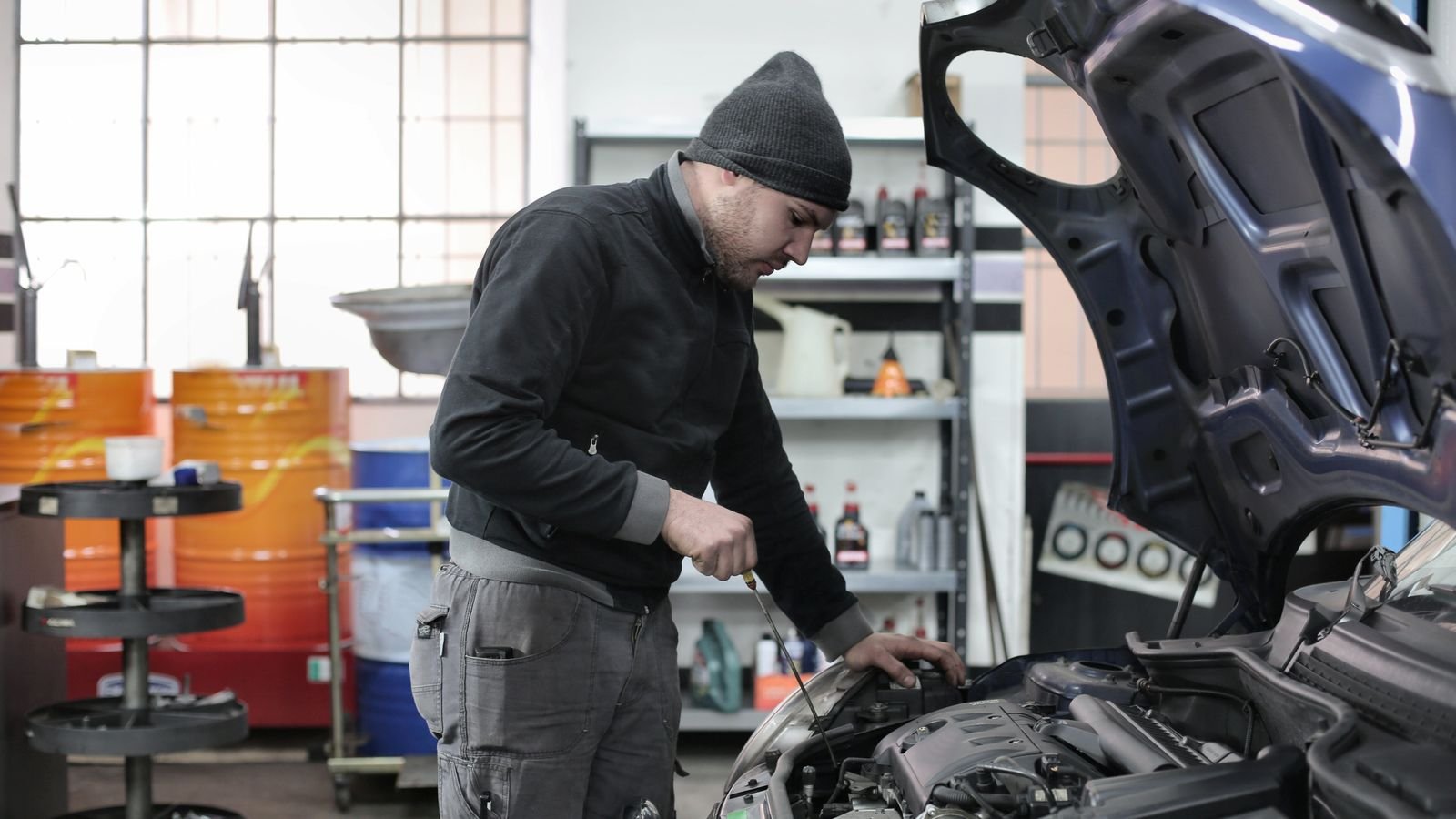 Mecânico verifica o motor de um carro com o capô aberto dentro de uma oficina