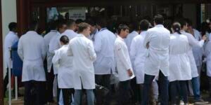 Candidatos de jaleco branco em fila na entrada do local de prova de exame para médicos