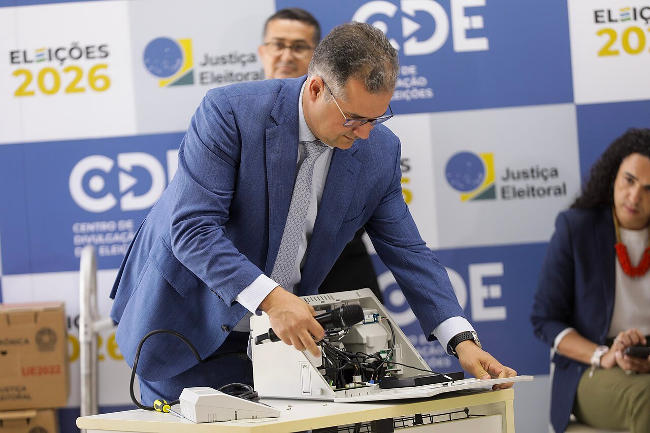 Tecnico abre urna eletronica diante de painel do Centro de Divulgacao das Eleicoes 2026