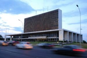Fachada do Palácio do Buriti, sede do governo do Distrito Federal, ao entardecer, com carros passando na via em primeiro plano