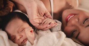 Mãe deitada ao lado de um bebê recém-nascido segura a mão da criança