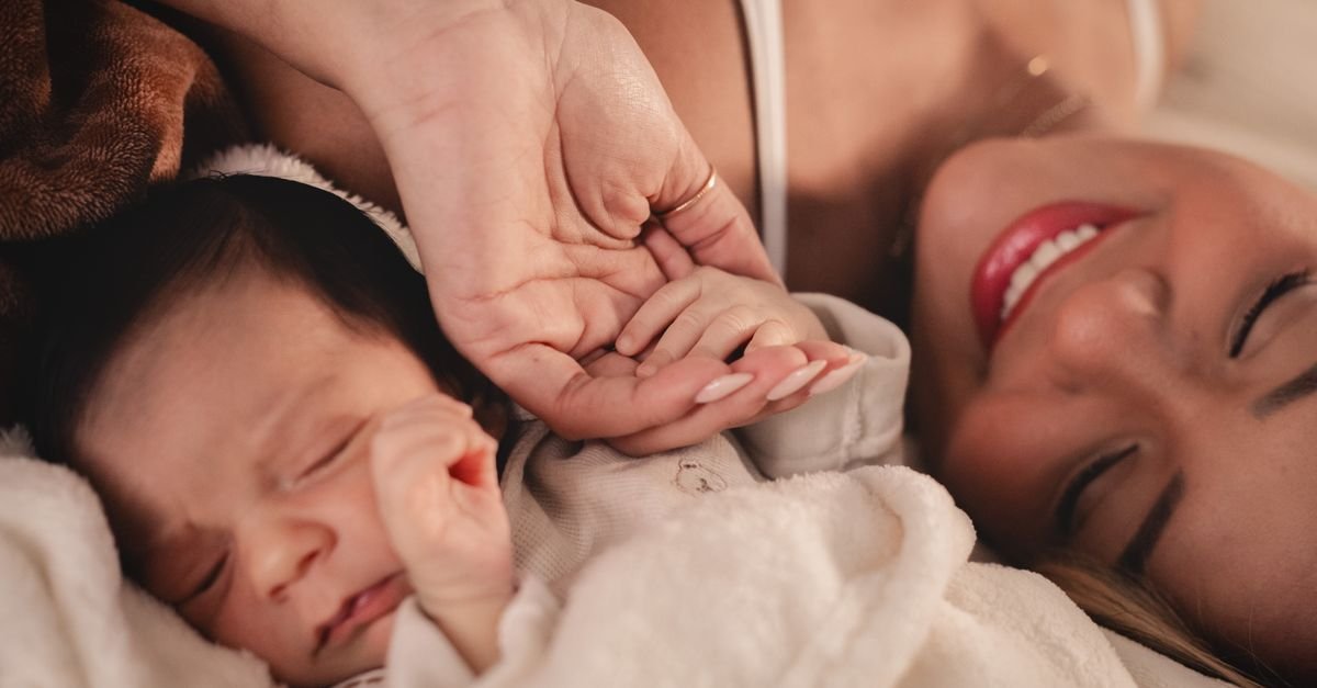Mãe deitada ao lado de um bebê recém-nascido segura a mão da criança