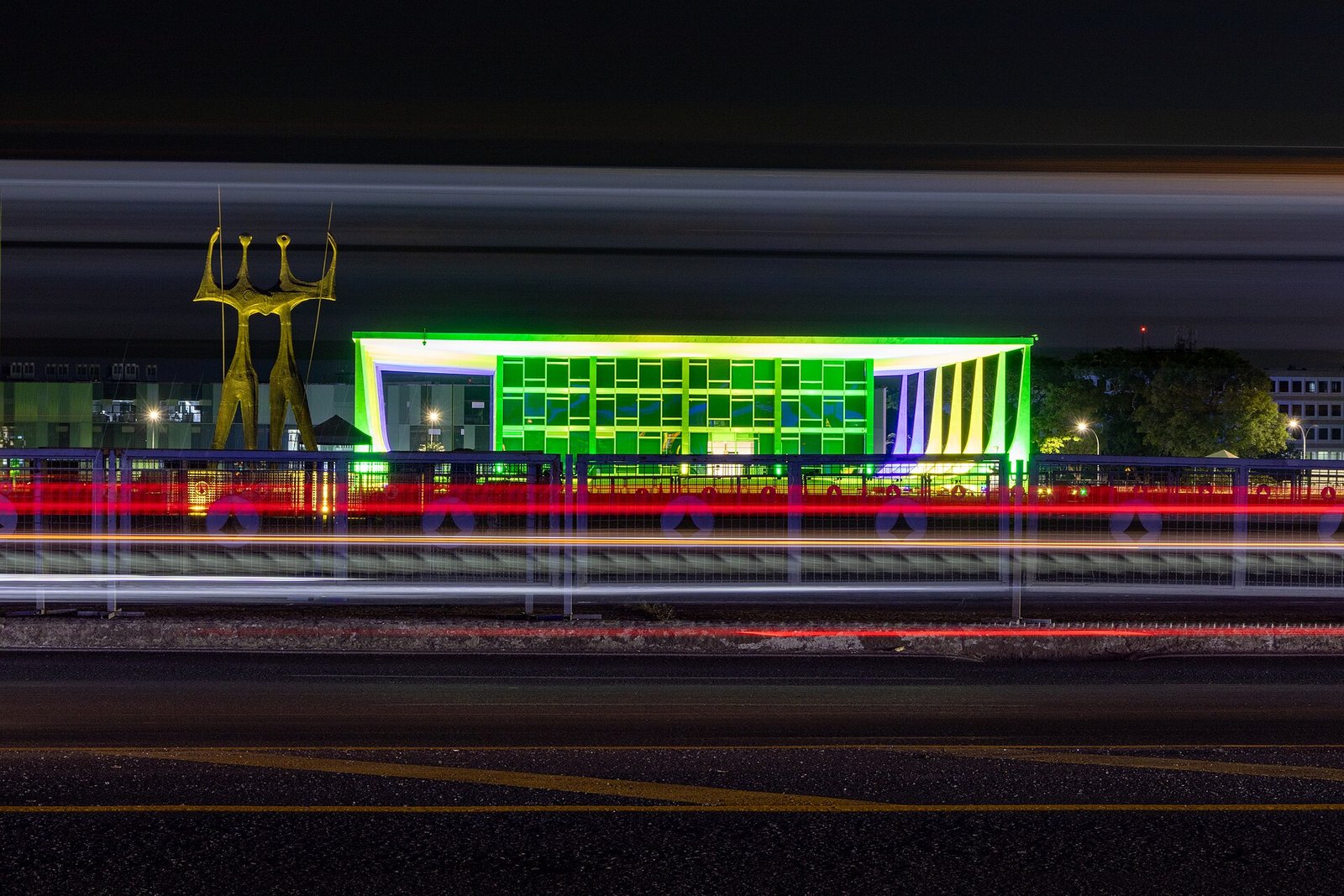 Fachada do Supremo Tribunal Federal iluminada à noite, com a escultura Os Candangos ao lado
