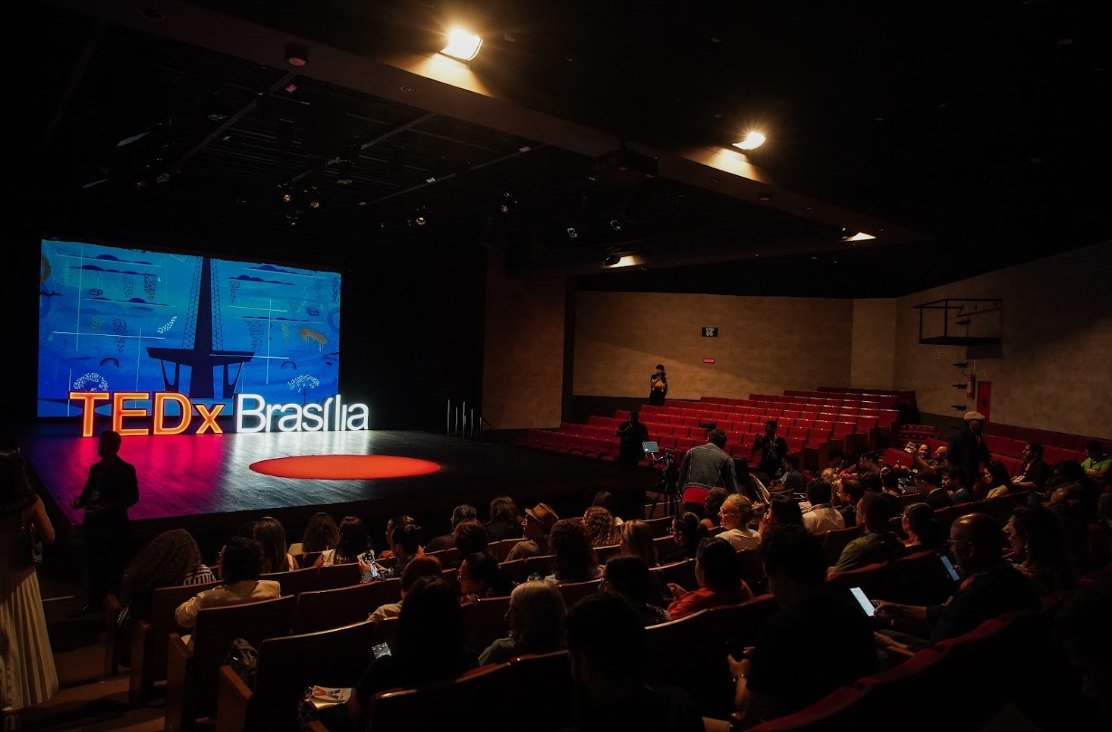 Plateia cheia diante de palco com letreiro TEDx Brasília e o círculo vermelho no chão