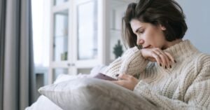 Mulher sentada em sofá segurando celular, com expressão pensativa