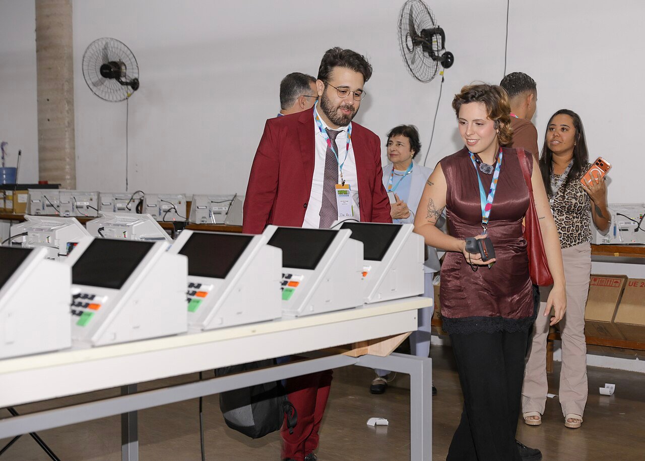Fileira de urnas eletronicas sobre mesa em sala de preparacao da Justica Eleitoral