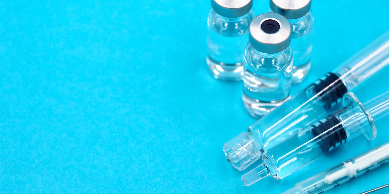 Frascos de vacina e seringas dispostos sobre superfície azul em close
