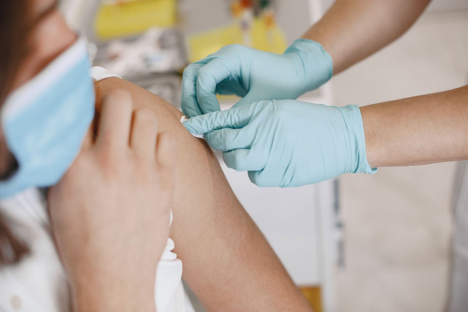Profissional de saúde com luvas azuis aplica curativo no braço de uma mulher após a vacinação