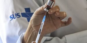 Profissional de saúde com jaleco do SUS prepara seringa a partir de frasco de vacina