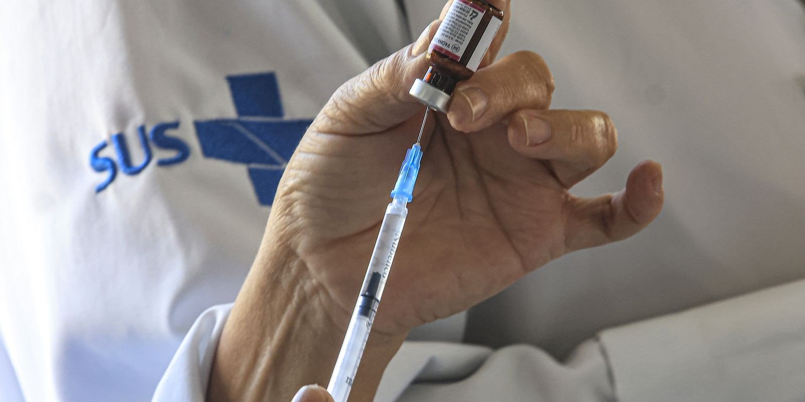 Profissional de saúde com jaleco do SUS prepara seringa a partir de frasco de vacina