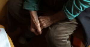 Mãos entrelaçadas de pessoa idosa sentada, em close