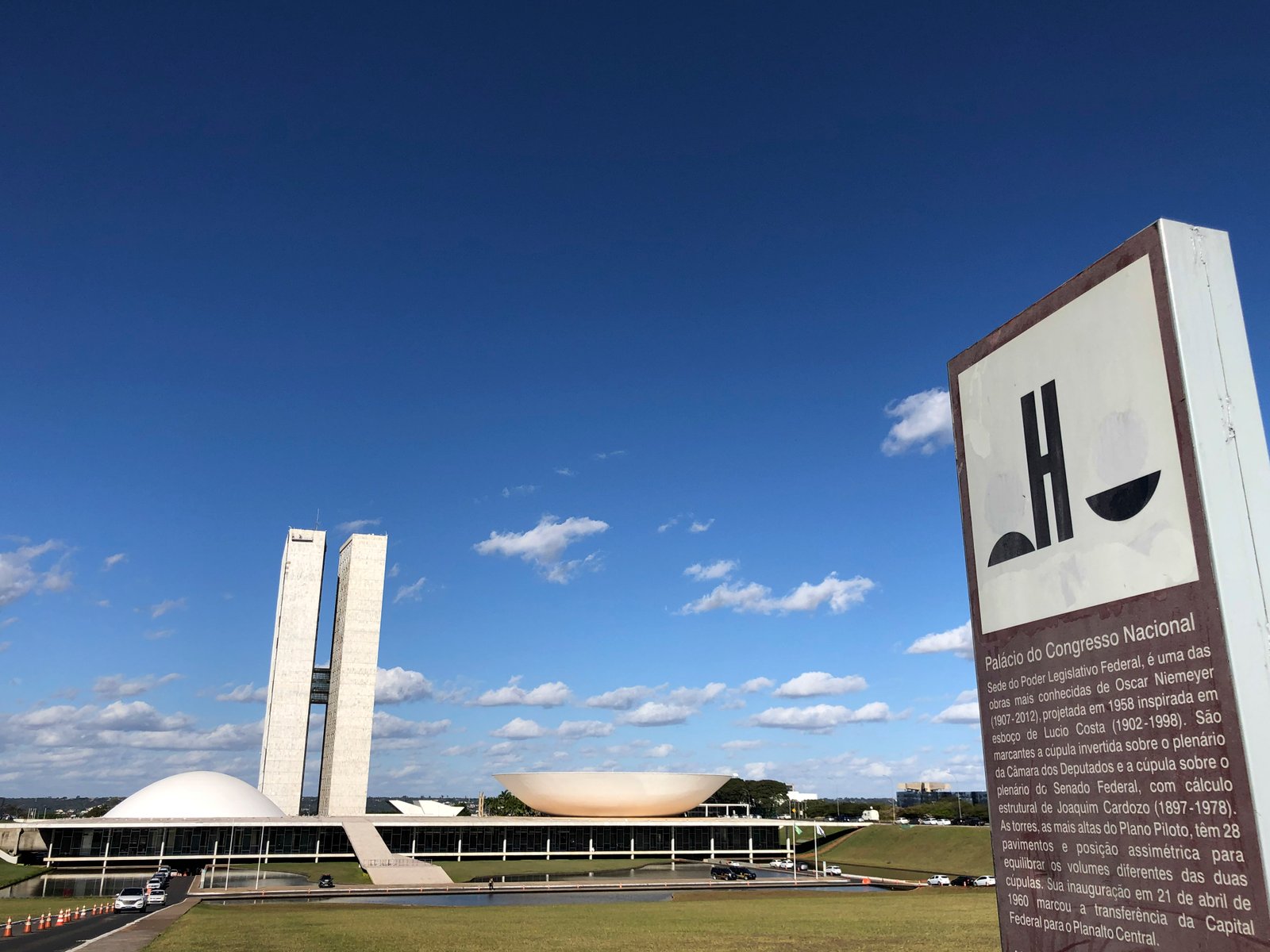 Palácio do Congresso Nacional visto da Esplanada, com as duas cúpulas e as torres, ao lado da placa informativa do prédio