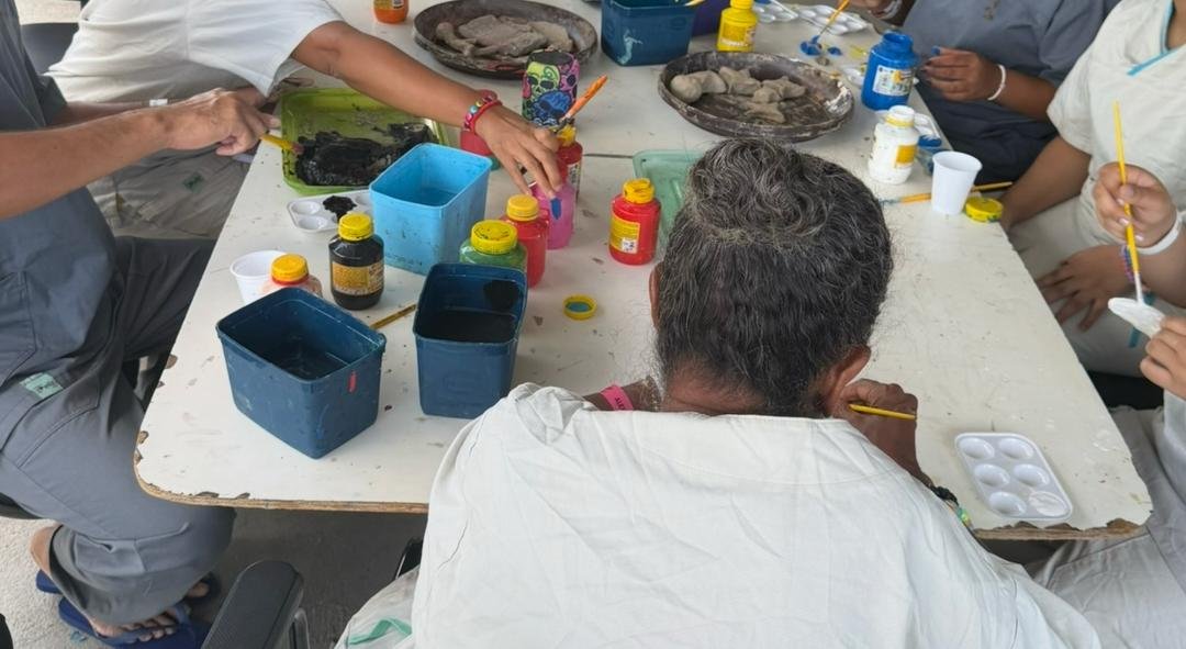 Pacientes e voluntários em volta de mesa com tintas e peças de argila no pátio da ala psiquiátrica