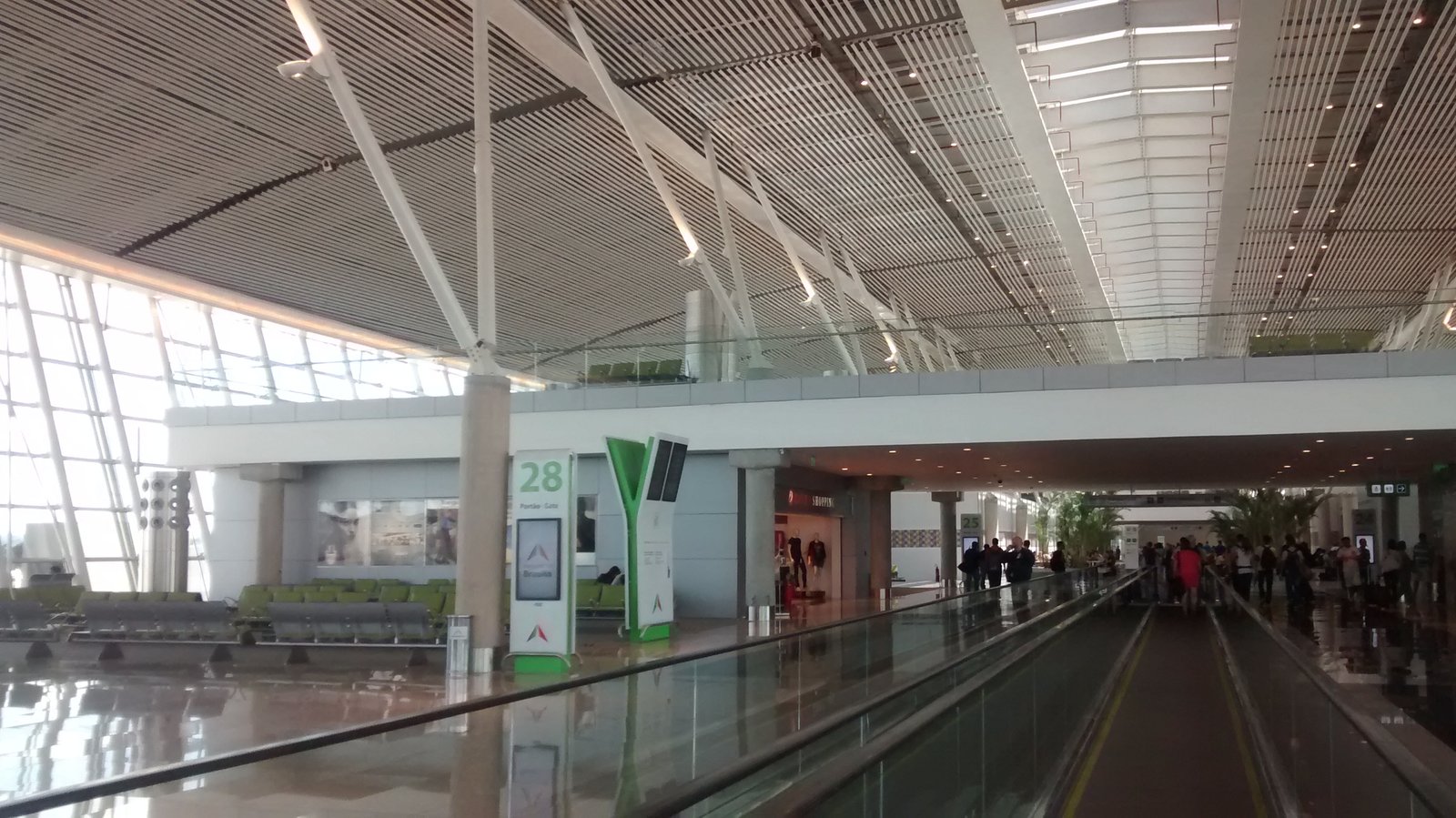 Saguão de embarque do Aeroporto de Brasília, com esteira rolante, poltronas vazias e a placa do portão 28