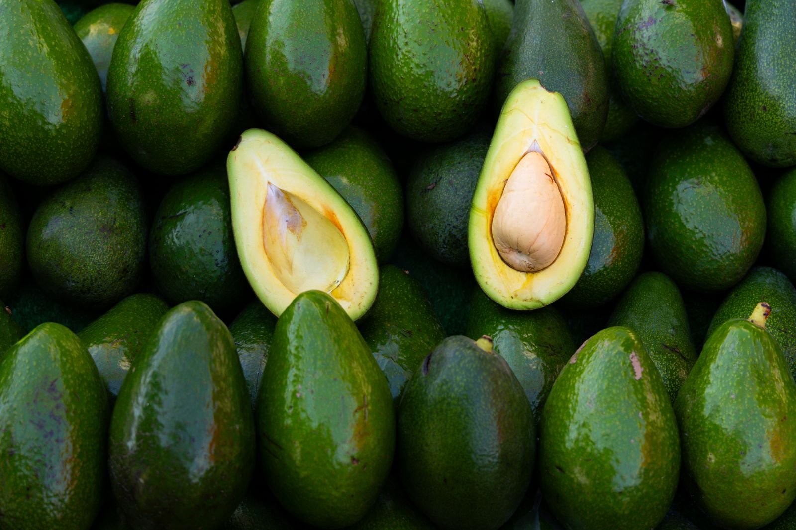 Abacates frescos empilhados, dois deles cortados ao meio mostrando o caroço