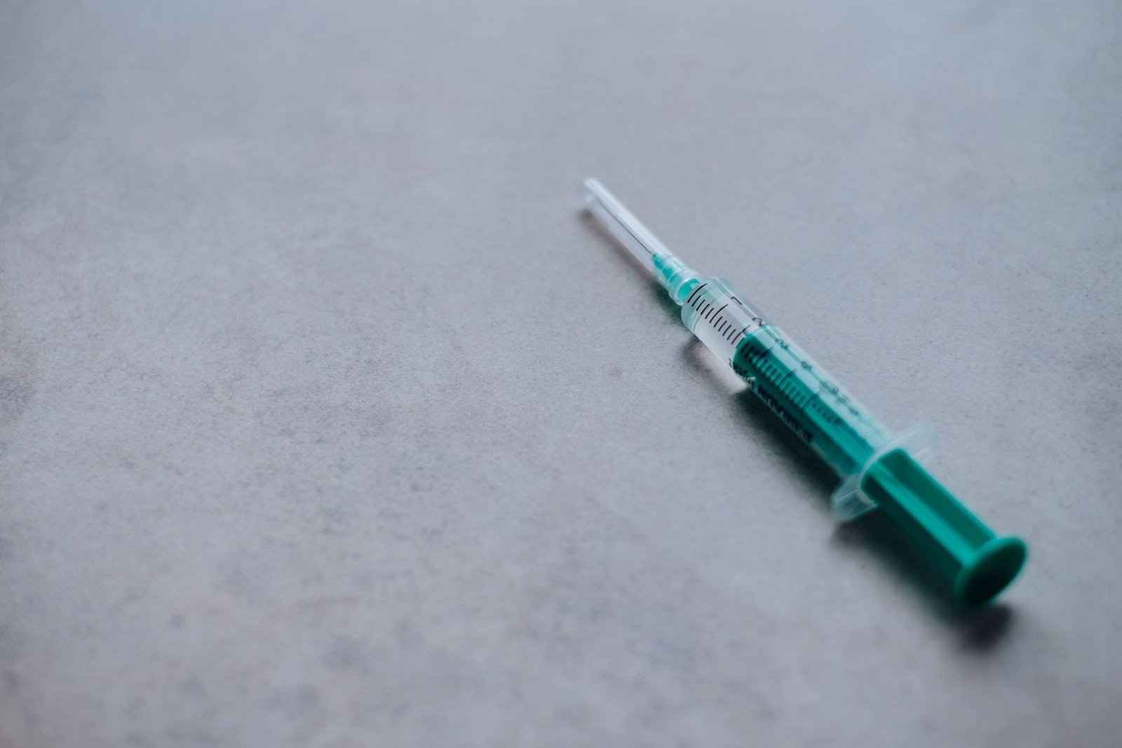 Seringa com êmbolo verde sobre superfície cinza, imagem ilustrativa de medicamento injetável