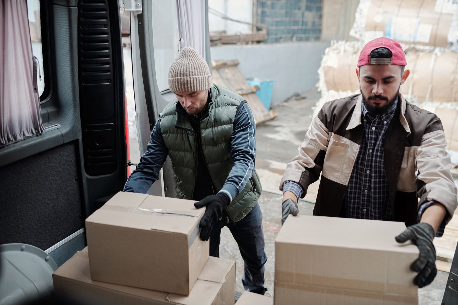 Dois trabalhadores descarregam caixas de papelão de uma van, em foto ilustrativa