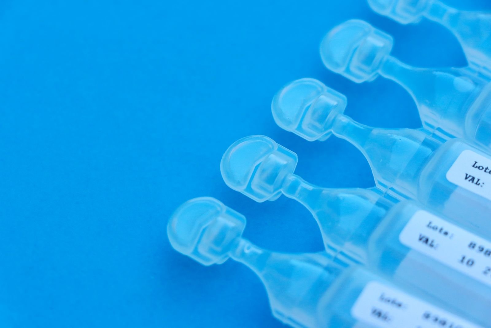 Ampolas plásticas transparentes com rótulo de lote e validade sobre fundo azul, imagem ilustrativa