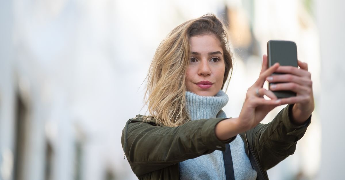 Jovem tira uma selfie com o celular na rua, em foto de arquivo