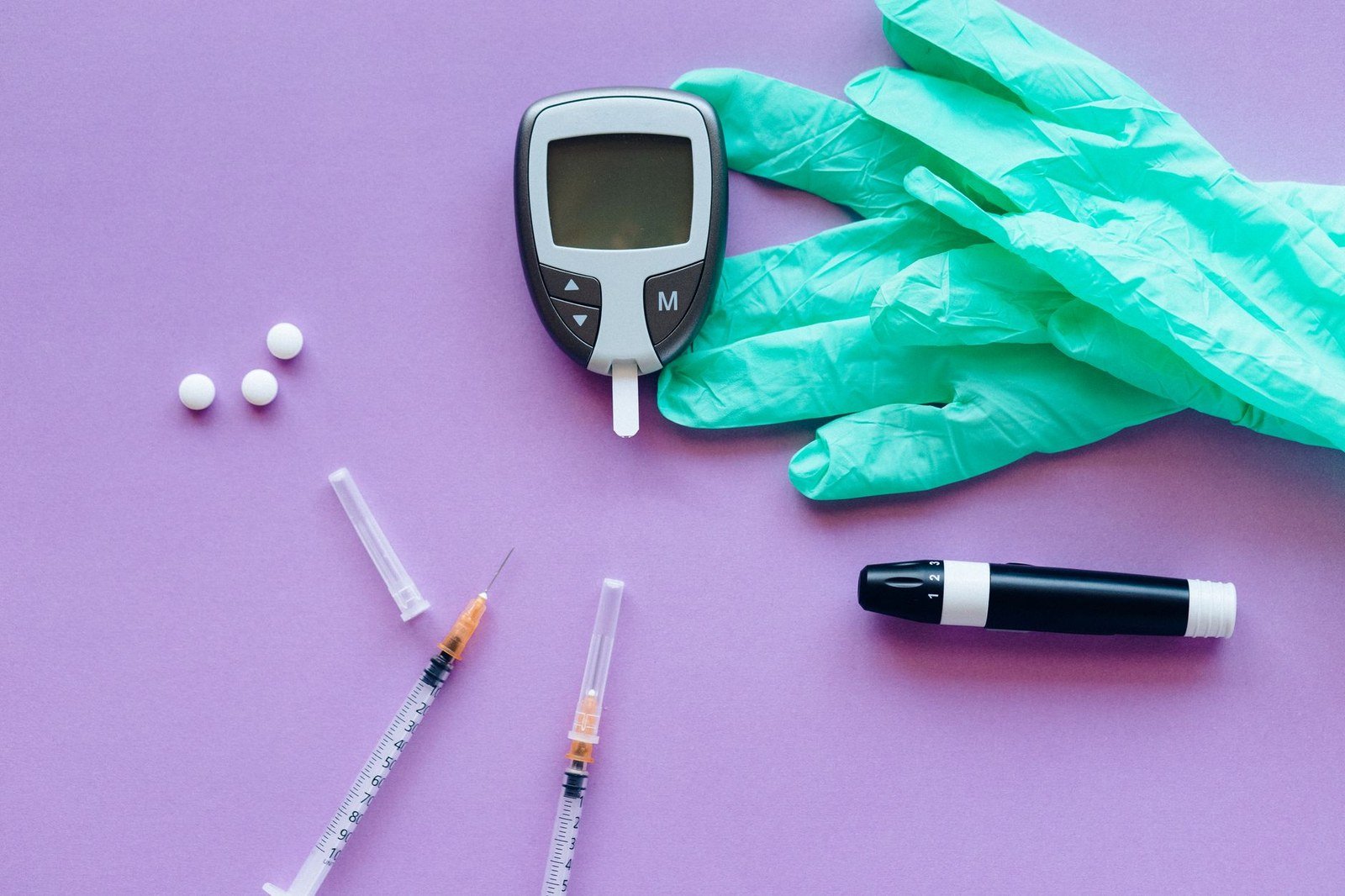 Glicosímetro, seringas e luvas sobre fundo roxo, em foto de arquivo sobre diabetes