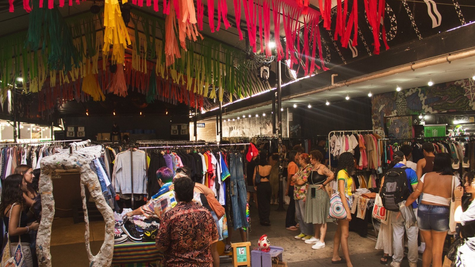 Araras com roupas de brechó e visitantes sob bandeirolas coloridas em edição do Ao Desapego