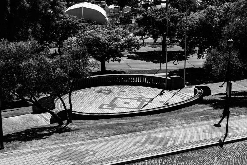 Praça urbana em preto e branco, com árvores, piso geométrico e área de convivência