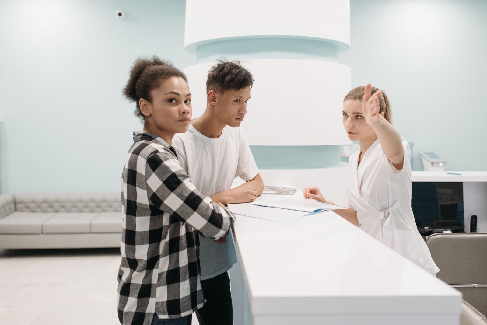 Duas pessoas no balcão de recepção de uma unidade de saúde recebem orientação de uma atendente, foto de arquivo