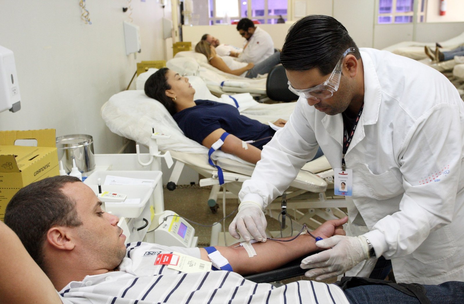 Doadores deitados em macas e profissional de saúde de jaleco preparando a coleta de sangue na Fundação Hemocentro de Brasília, em foto de arquivo
